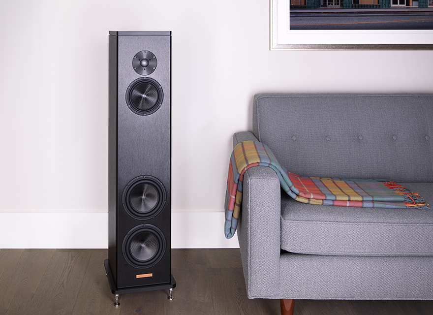 Magico A3 Loudspeaker in living room with grey sofa on dark wood floor.